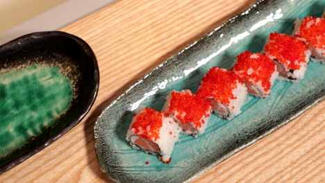 delicious sushi rolls in a plate topped with orange roe - high angle panning shot, slow motion