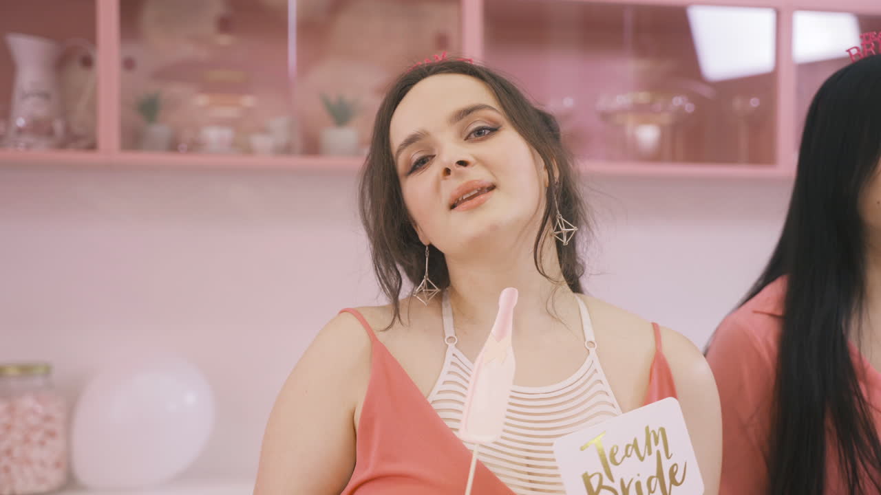vista de cerca de una mujer morena con tocados y sosteniendo una decoración de cartón bailando en una habitación rosa celebrando una despedida de soltera 1