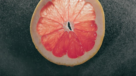 grapefruit slice splashed by strong water droplet mist in slow motion with backlit black background