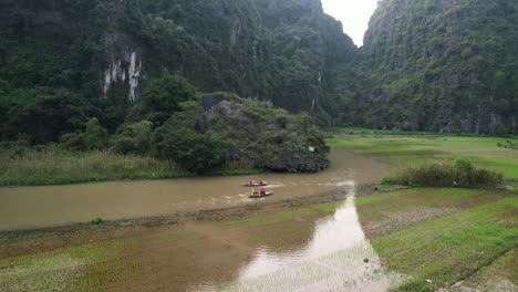 Menschen,-Die-Auf-Sampan-Booten-Auf-Dem-Wogenden-Ngo-Dong-Fluss-In-Der-Majestätischen-Landschaft-Von-Ninh-Binh,-Vietnam,-Fahren-–-Niedrige-Luftaufnahme-Im-Orbit