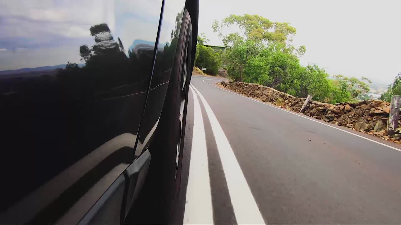 POV dall'auto: Ruota anteriore destra su strada asfaltata in discesa verso la città
