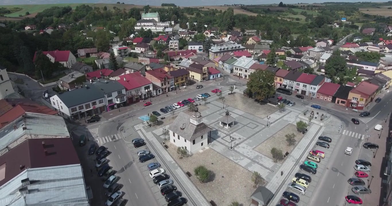 Letecký 4K záběr malebného náměstí za slunečného letního dne, s kostelem, poli a stromy v pozadí.