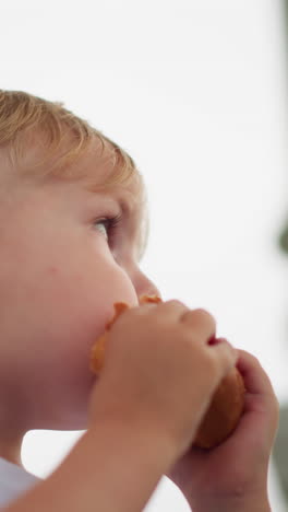 a young child is captured holding a snack near their mouth, seemingly pausing mid-bite while glancing around with curiosity