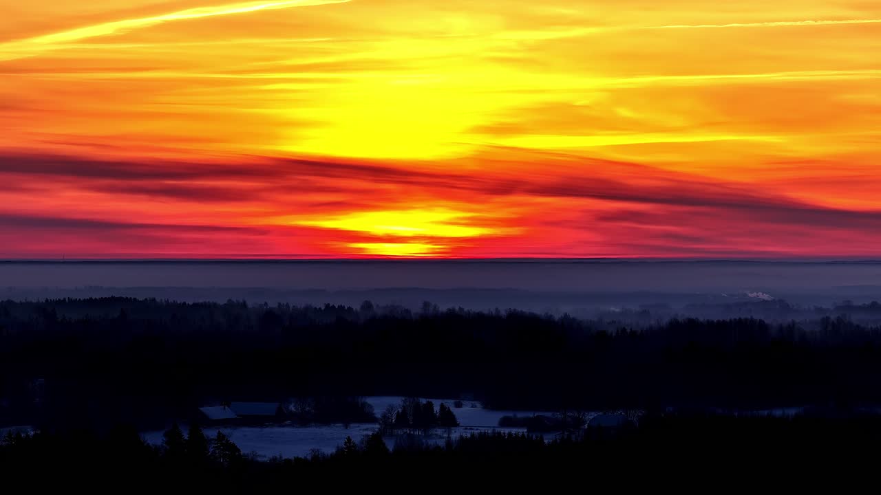 Ein dunkel rot-orangefarbener Himmel in der Dämmerung über einer weiten Waldlandschaft.