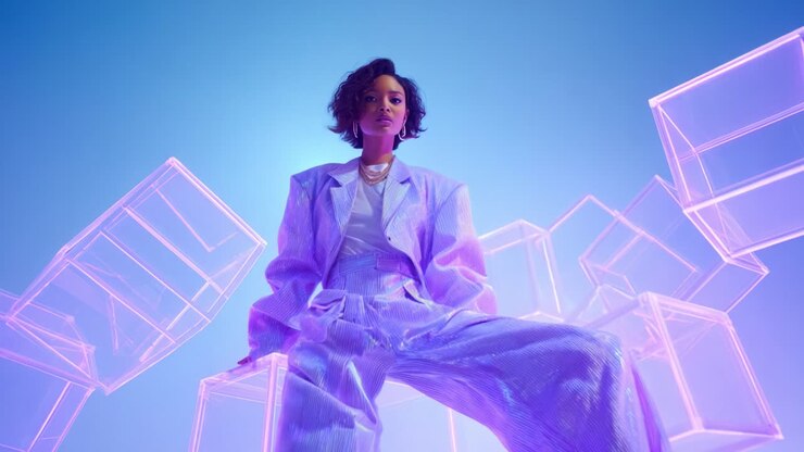 En fantastisk model i et futuristisk outfit, omgivet af æteriske, transparente kuber, der indtager en dristig positur mod en levende blå baggrund, som forstærker den slående visuelle tiltrækningskraft og moderne æstetiske atmosfære