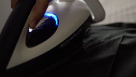 slow motion close-up shot of an individual pressing a pair of pants using an electric iron and an ironing board