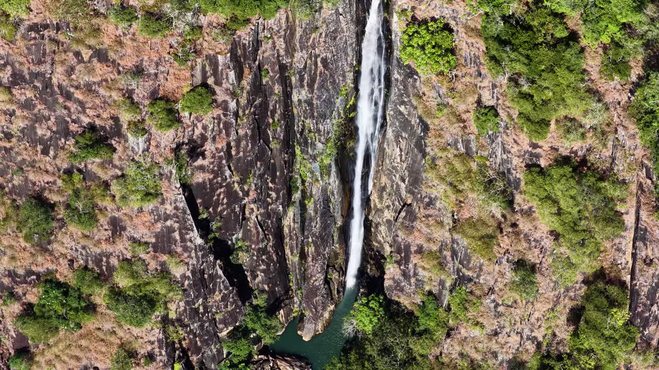 Drone captures a stunning waterfall cascading through dense rainforest in Port Douglas, Queensland, under bright daylight