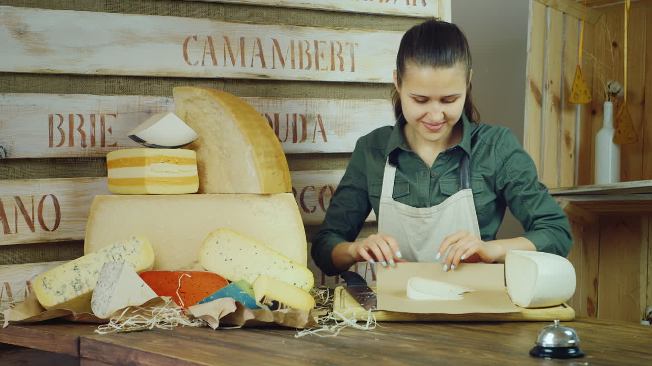 una joven vendedora empaca queso y luego sonríe a la cámara de video hd