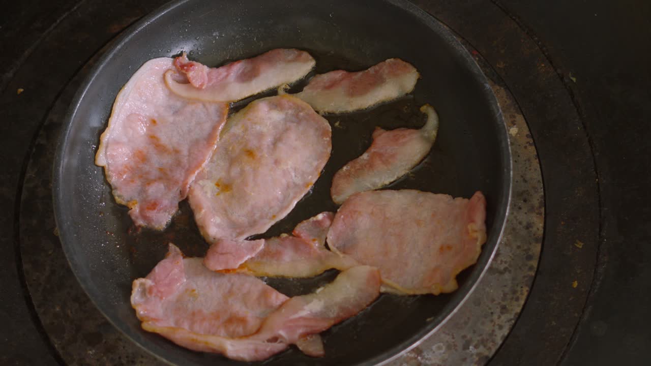 Overhead View of Smoked Bacon Slices Sizzling in Hot Frying Pan on Stove. Hot Morning Breakfast Food.