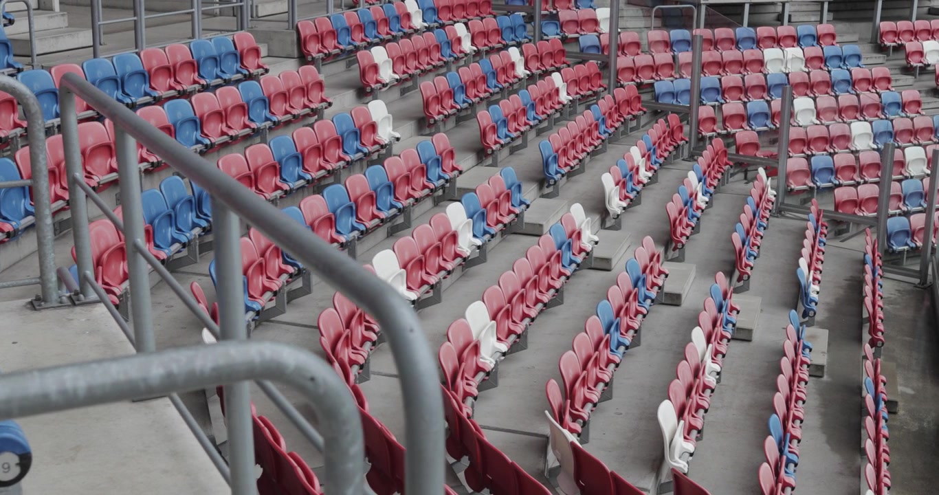 Toma dinámica con gimbal de gradas vacías en un moderno estadio de fútbol con asientos rojos, azules y blancos en Europa Central, 4K