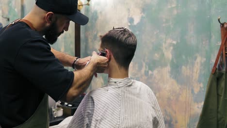 barbero barbudo creando una línea recta usando un cortador eléctrico en la sien de un hombre. joven hombre caucásico guapo cortándose el cabello