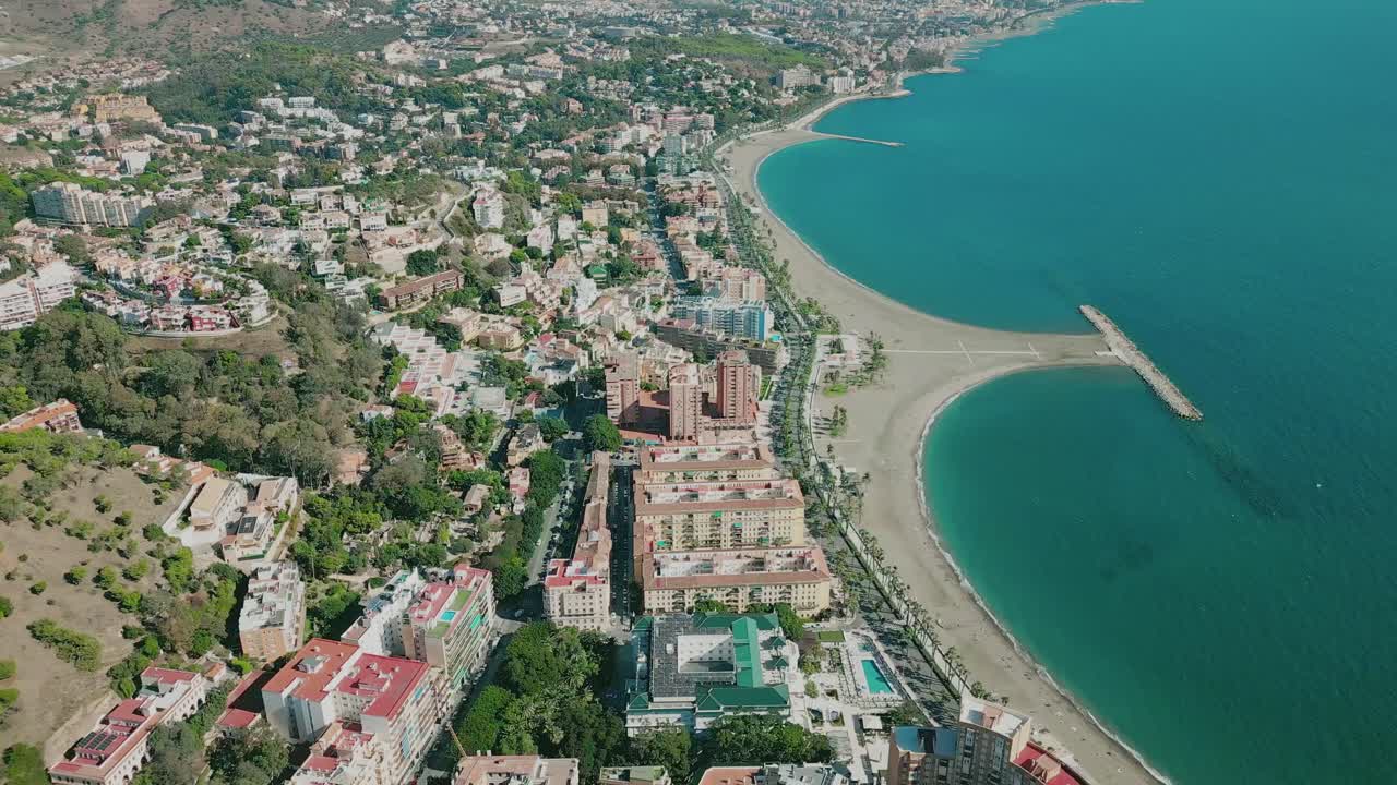 Aerial shot of Playa de la Malagueta, Málaga, Spain, golden sandy beach, calm Mediterranean waves, and sunny urban coastline
