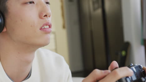 Close-up-of-asian-boy-wearing-headphones-playing-video-games-sitting-on-the-couch-at-home