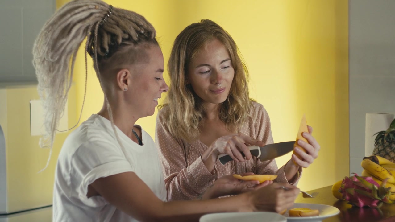 Two Women Preparing and Eating Fresh Mango in a Kitchen