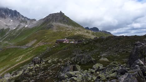 sobrevuelo aéreo montañas rocosas y cubiertas de musgo de suiza con cabaña en el fondo durante el día nublado