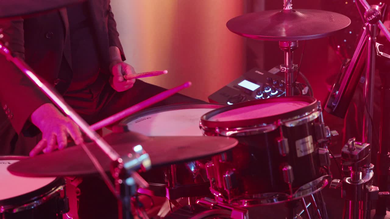 Batterista che suona una batteria sotto un'illuminazione rossa durante una performance dal vivo.