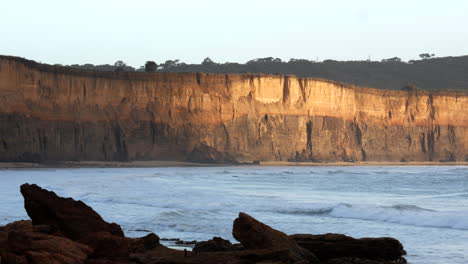 morning sun reflecting on the sandstone cliff face of an eroded australian beach