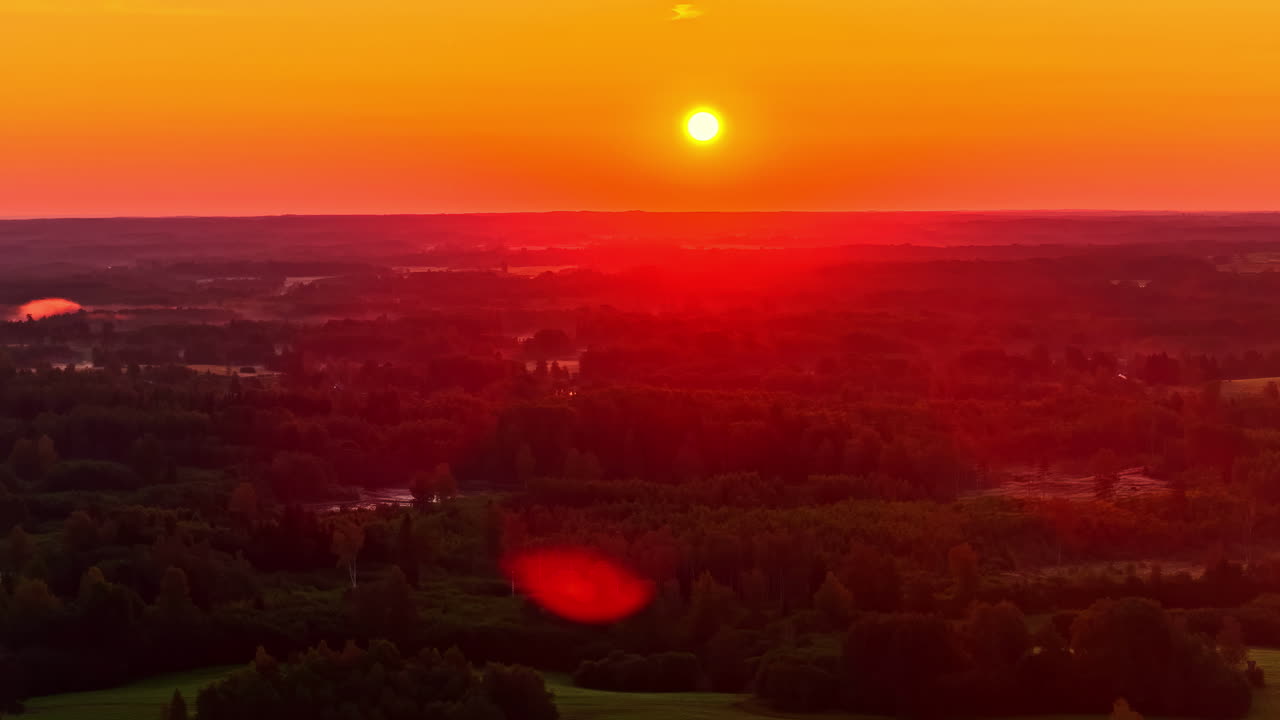 A captivating and vibrant red-orange sunset creates a dramatic sky and golden light over a vast, dense, dark green forest and sprawling rural landscape