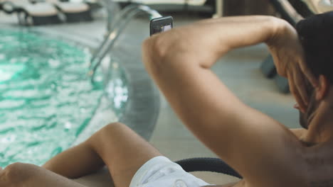 hombre joven de primer plano posando en la cámara del teléfono cerca de la piscina en cámara lenta.