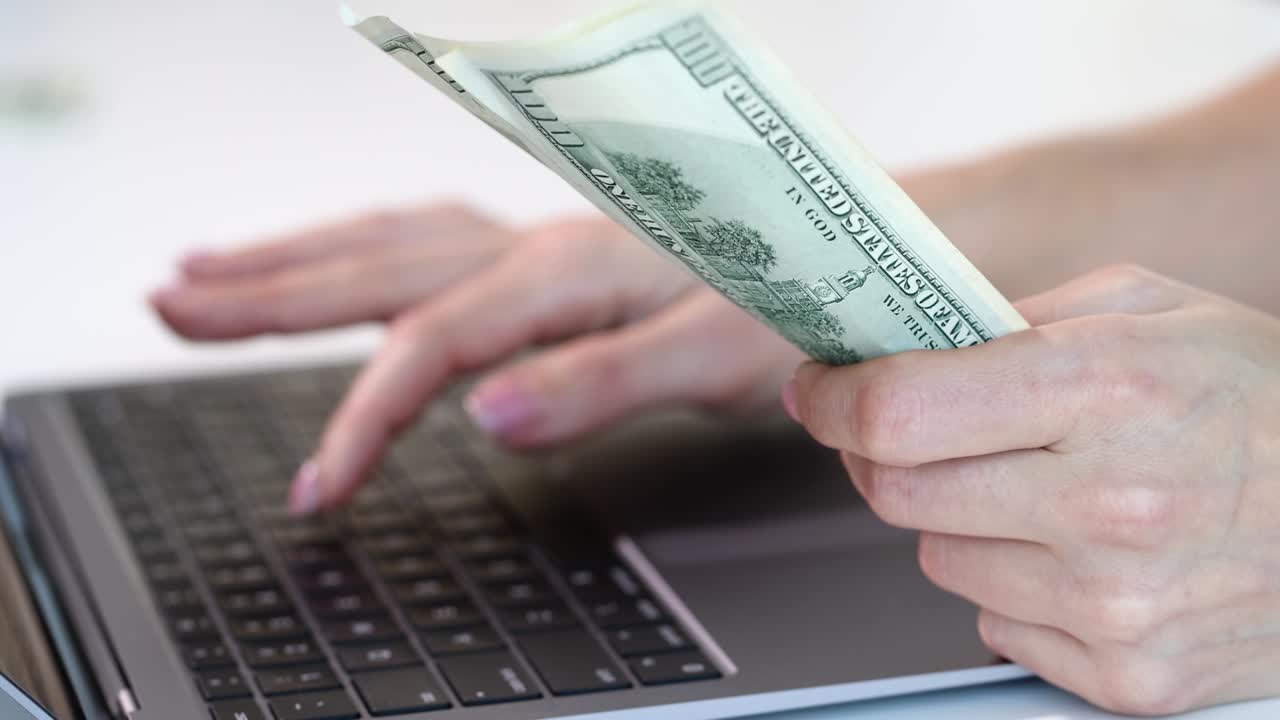 доллары в женской руке и работать на компьютерной клавиатуре