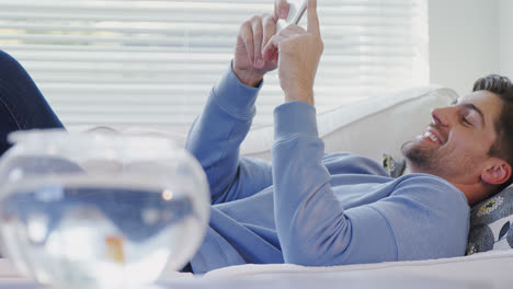 gold fish bowl and man lying on sofa using his mobile 4k 4k