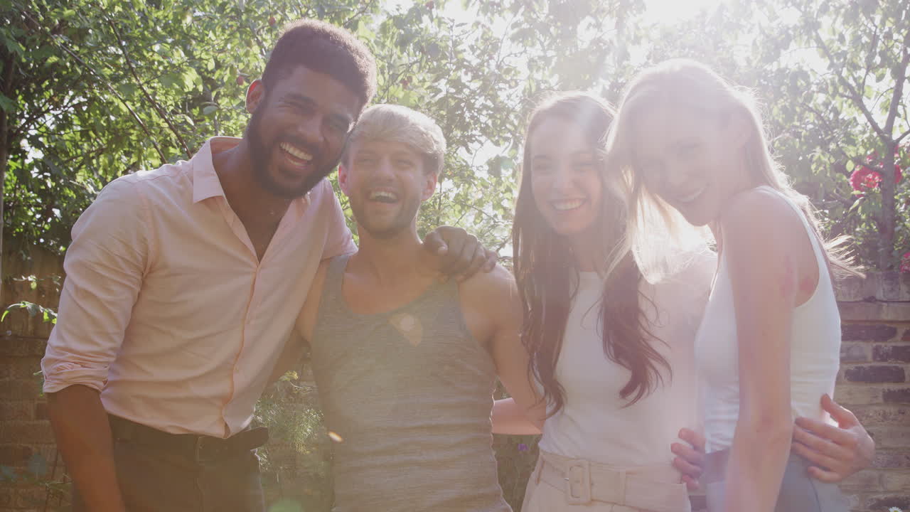 Retrato de amigos gays masculinos e femininos em casa no jardim, juntos contra o sol forte