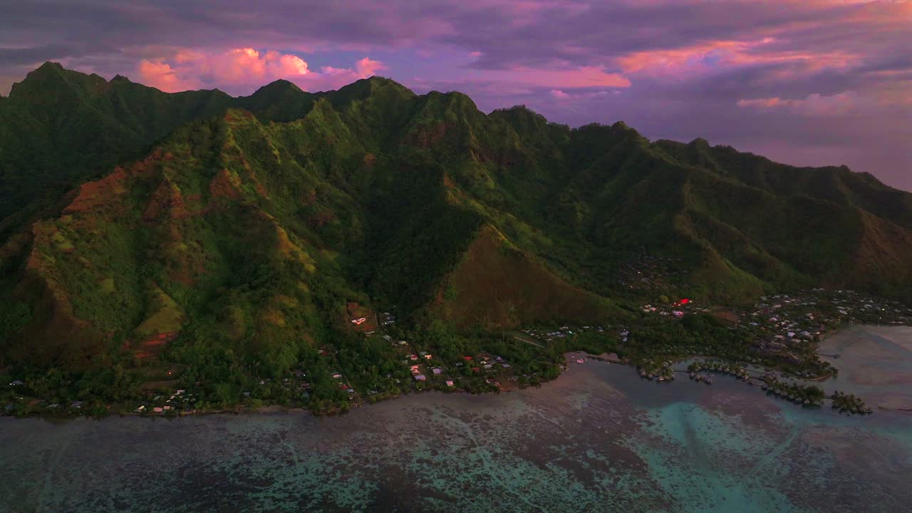 Deep purple pink sunset at Moorea island Cooks Opunohu bay French Polynesia aerial drone bright blue lagoon coral reef Mount Mauaroa Tohivea Rotui jagged peaks Haapiti Paopao Pacific Ocean forward