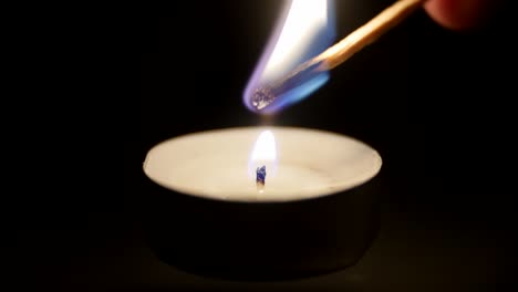 close-up of a match lighting a candle against a black background