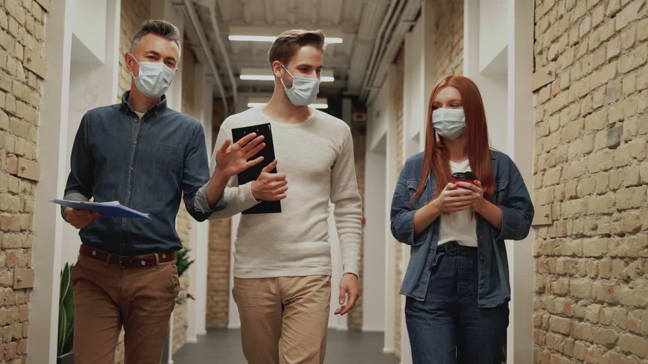 Business men and woman go to a work meeting during the Coronavirus pandemic. People with face mask walking towards the camera.