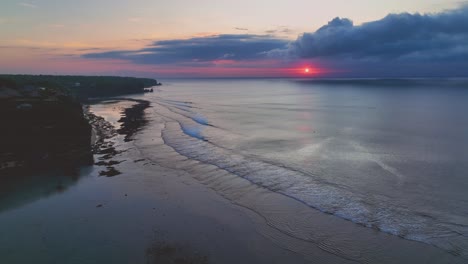 Estableciendo-Tomas-De-Drones-De-Los-Acantilados-De-Piedra-Caliza-Desde-La-Playa-De-Bingin-Hasta-Uluwatu,-Con-Suaves-Olas,-Océano-Abierto-Y-Puesta-De-Sol-Rosa-A-Través-De-Las-Nubes