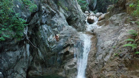 young man head jumps into water from rocky waterfall cliffs, aerial