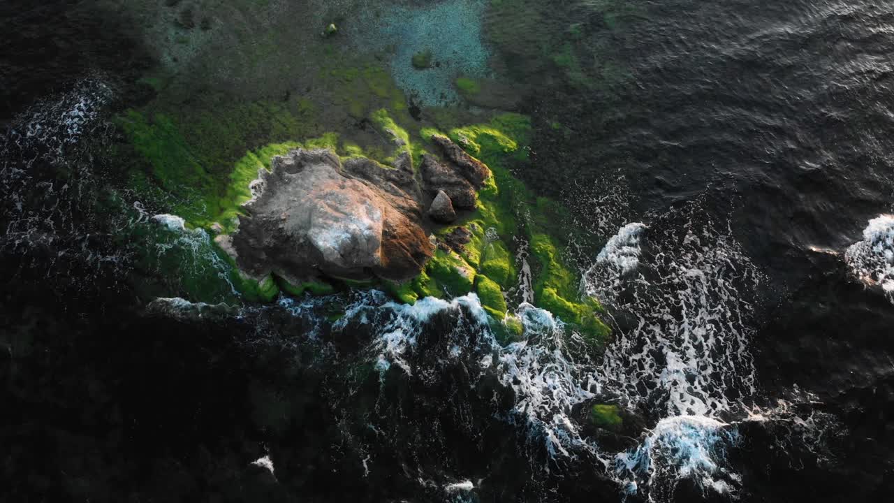 Arc aerial shot over rock in the sea at sunset, bright colors and dark water