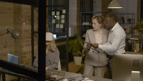 woman at desk in the office wearing virtual reality glasses while a woman and man is controlling her with tablet