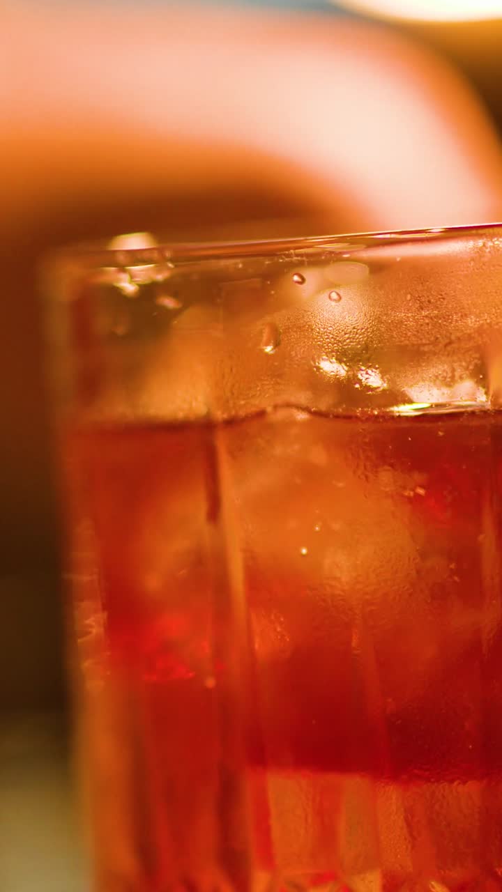 Primo piano estremo di un bicchiere da cocktail di cristallo riempito con liquido ambrato e cubetti di ghiaccio