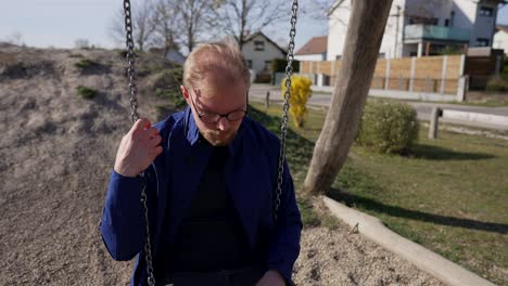 depressed sad caucasian man swinging on swings outside, close up