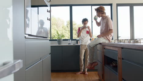 happy diverse gay male couple drinking coffee in kitchen at home, slow motion, copy space