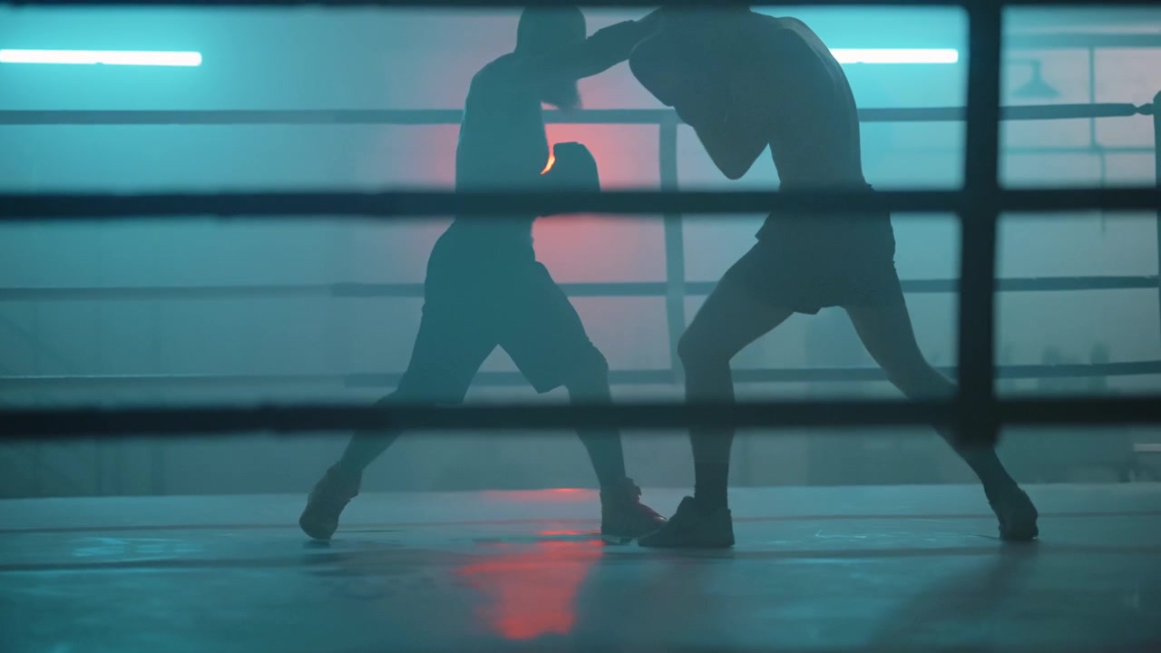 Sagome di due pugili che si allenano in un ring fumoso con luci al neon