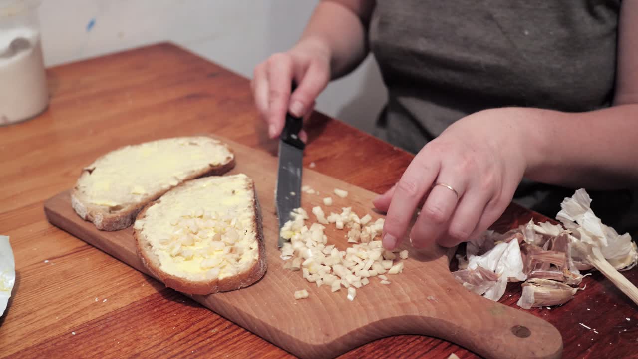 Woman's hands puts garlic on a slice of bread spread with butter