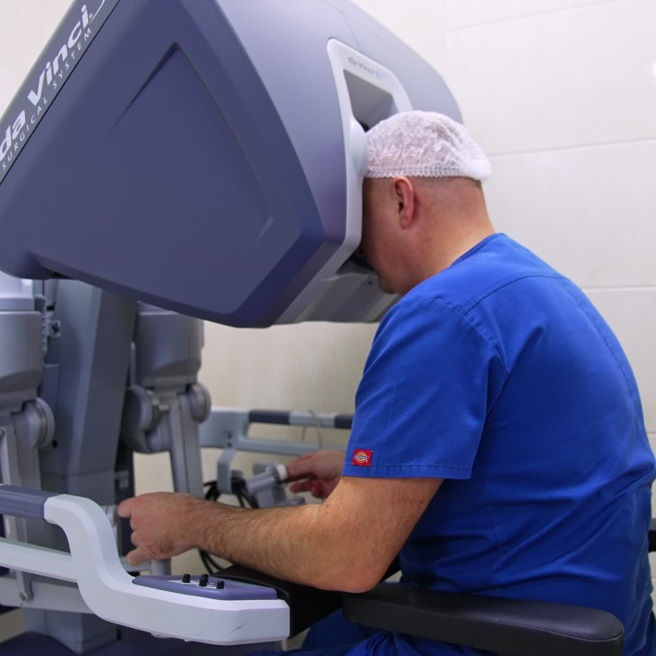 Experienced surgeon operating the technological Da Vinci robot in modern clinics. Uniformed specialist in blue uniform sitting at equipment looking at binoculars