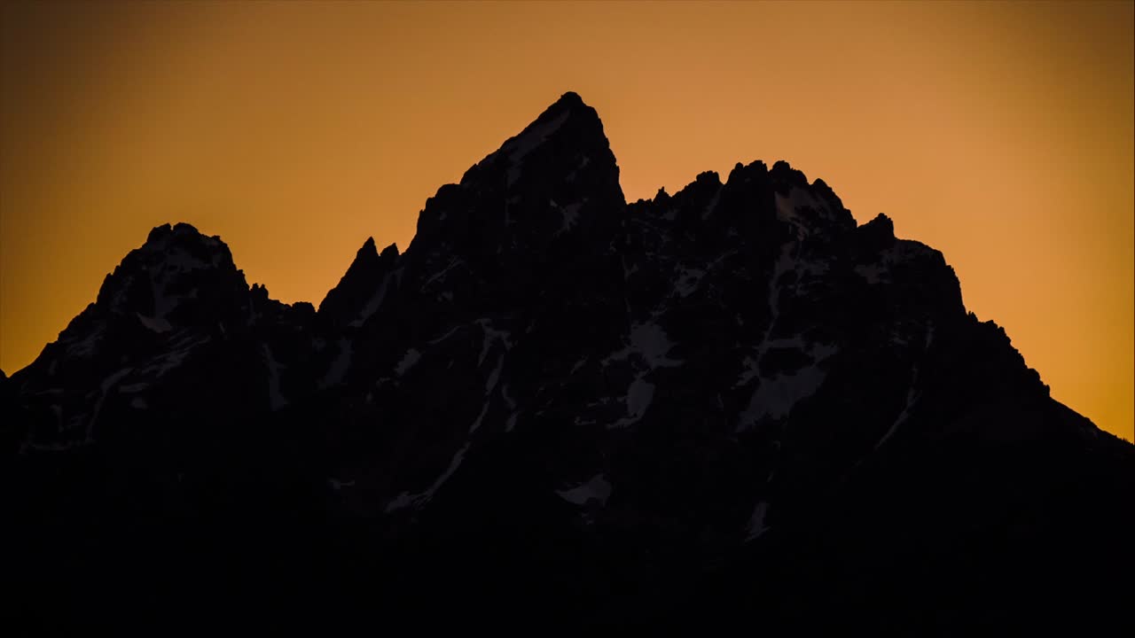 lapso de tiempo de una gran montaña que se desvanece con la puesta de sol dejando la silueta con un fondo naranja