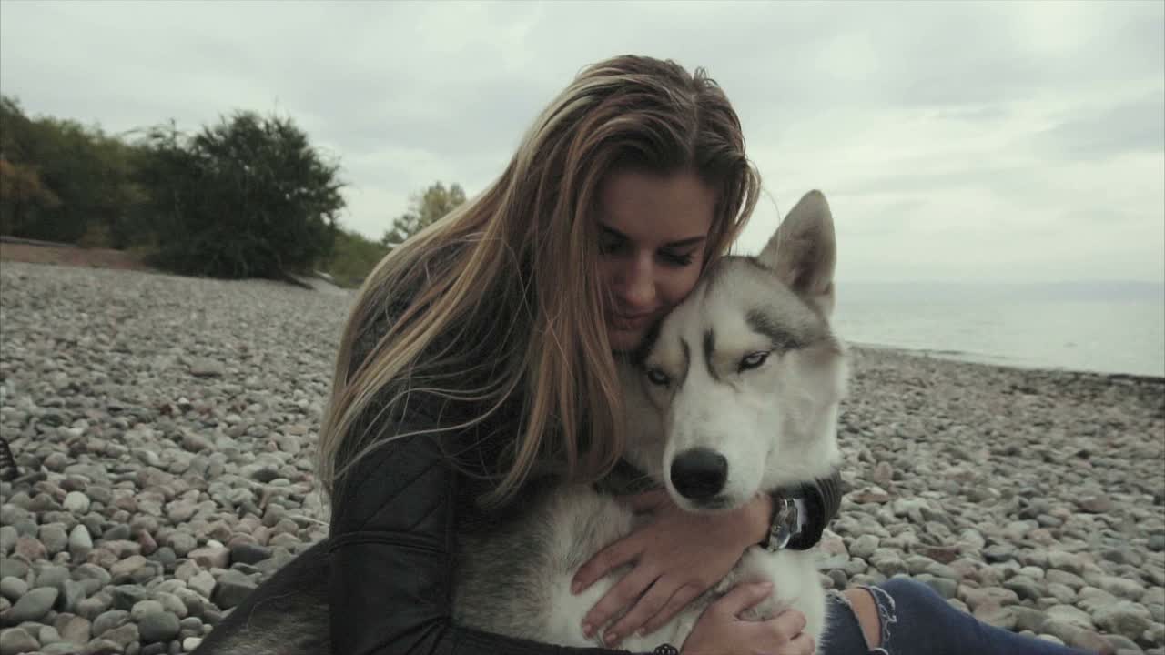 Woman hugging a husky dog on a pebble beach near a lake