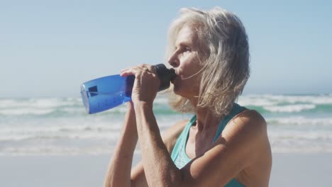 mujer mayor bebiendo agua en la playa