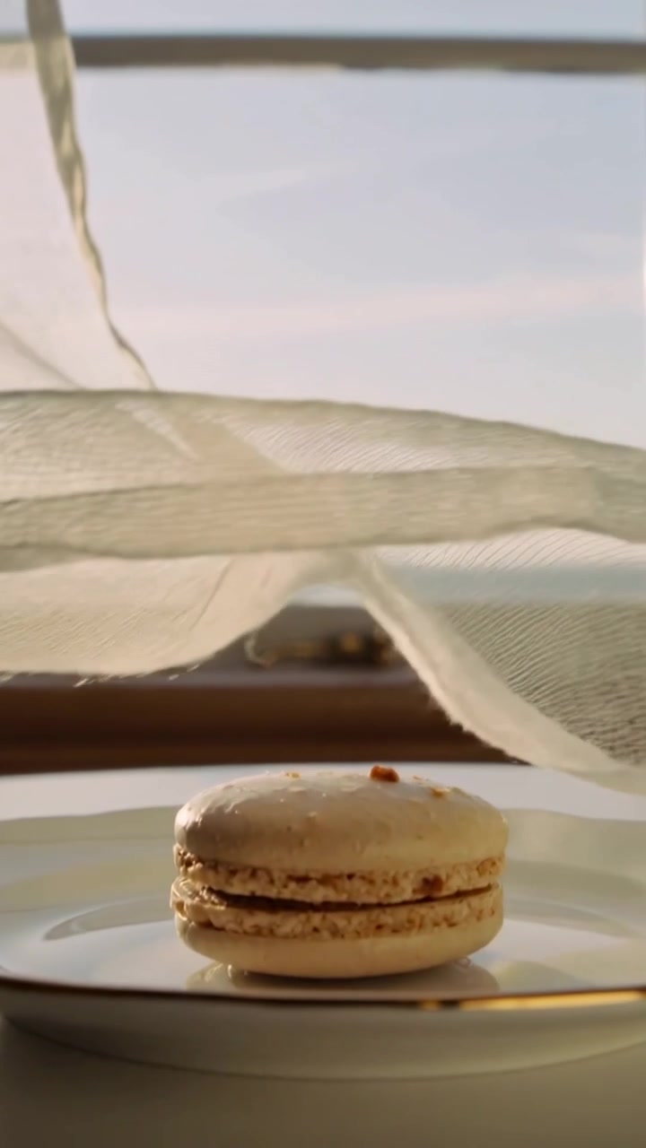 Vertical video: Billowing curtain lifting by breeze on sill by sea, draping macaron on gold plate
