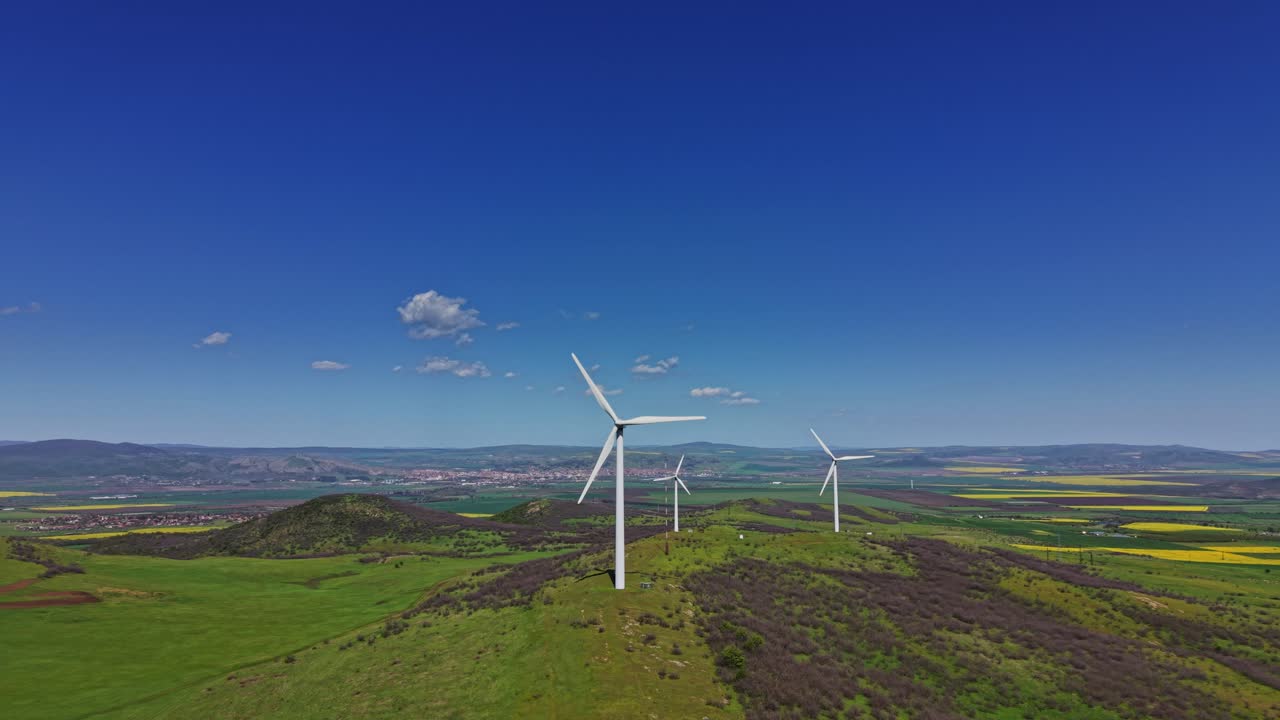 Pale eoliche su una collina verde sotto un cielo blu vicino a una città