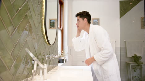 focused biracial man inspecting hair and face in bathroom mirror, copy space, slow motion