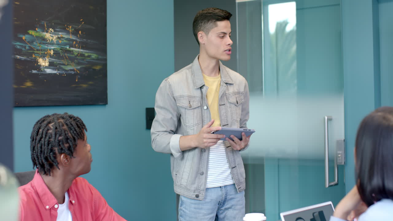 Presenting ideas in meeting, young man holding tablet while colleagues listen attentively
