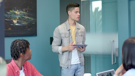 presenting ideas in meeting, young man holding tablet while colleagues listen attentively