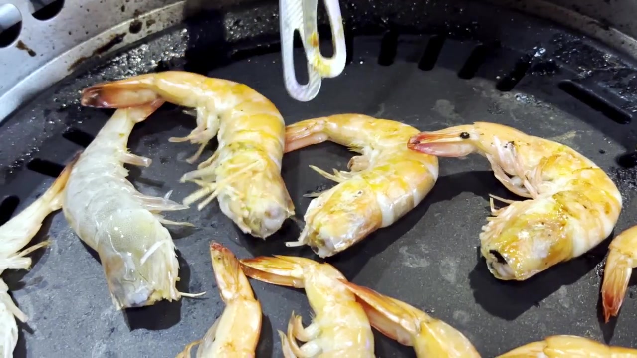 Primo piano di gamberi freschi che sfrigolano su una padella calda da barbecue, catturando frutti di mare succosi, vapore che sale e deliziosi sapori grigliati in una scena di cucina.