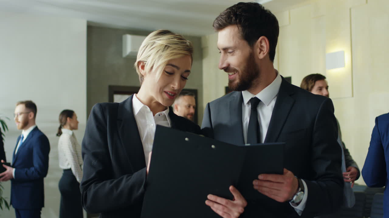 Caucasian businesswoman with a folder of documents in hands talking and discussing something with a businessman who holding a tablet during a break in a conference hall