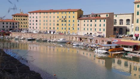 Pequeños-Barcos-De-Motor-Amarrados-En-Un-Canal-En-La-Ciudad-De-Livorno-En-Toscana-Y-Edificios-Típicos-En-El-Fondo